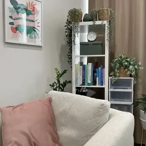 A cozy living room featuring a couch, a bookshelf filled with books, and several green plants for decoration.