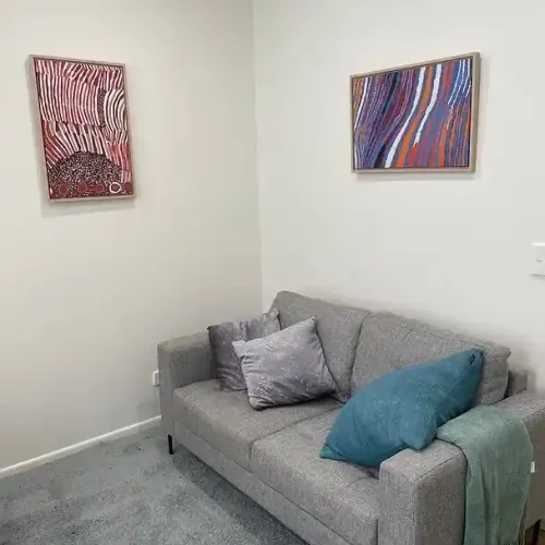 A grey couch in a room adorned with two paintings on the wall, creating a cozy and artistic atmosphere.